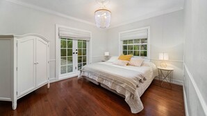 A bedroom with a large bed, a wardrobe, a chandelier, and a window with a view of greenery. - Stylish villa in the heart of all fun in Miami (Miami)