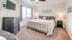 Ein Schlafzimmer mit Bett, Deckenventilator, Wand-Fernseher, Fenster und Nachttisch mit Lampe.
