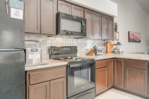 A kitchen with dark wooden cabinets, a stainless steel refrigerator, a microwave, a stove, and a dishwasher.