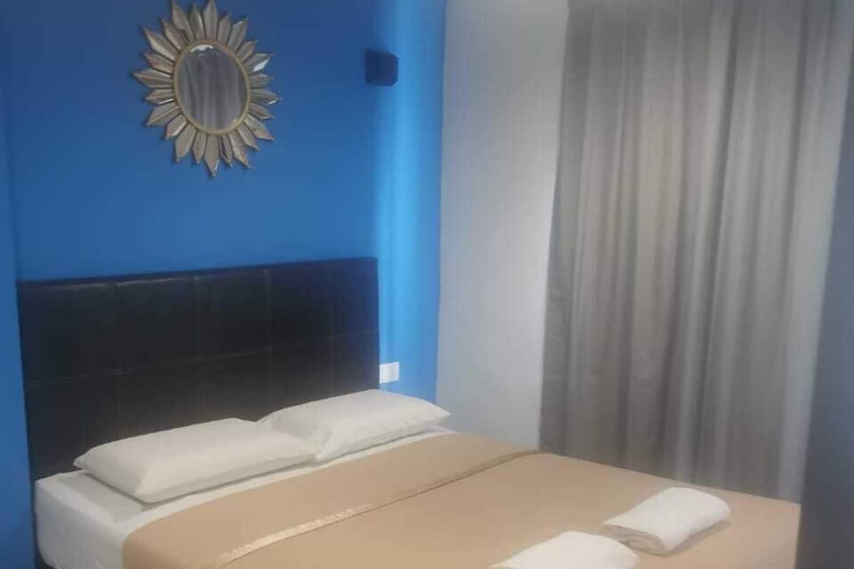 A hotel room with a single bed, a headboard, a mirror, and a curtain.