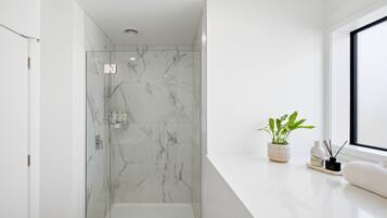 Un baño moderno con cabina de ducha de vidrio, paredes de mármol, encimera blanca y ventana.
