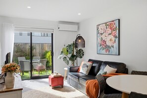 Ein modernes Wohnzimmer mit einer Ledersofa, einem Esstisch und einem großen Fenster mit Blick auf einen Garten.