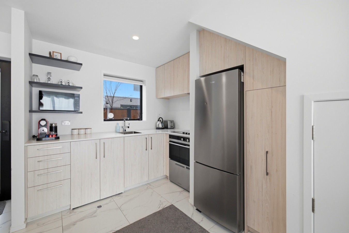 A modern kitchen with a stainless steel refrigerator, a built-in oven, and a window above the sink.