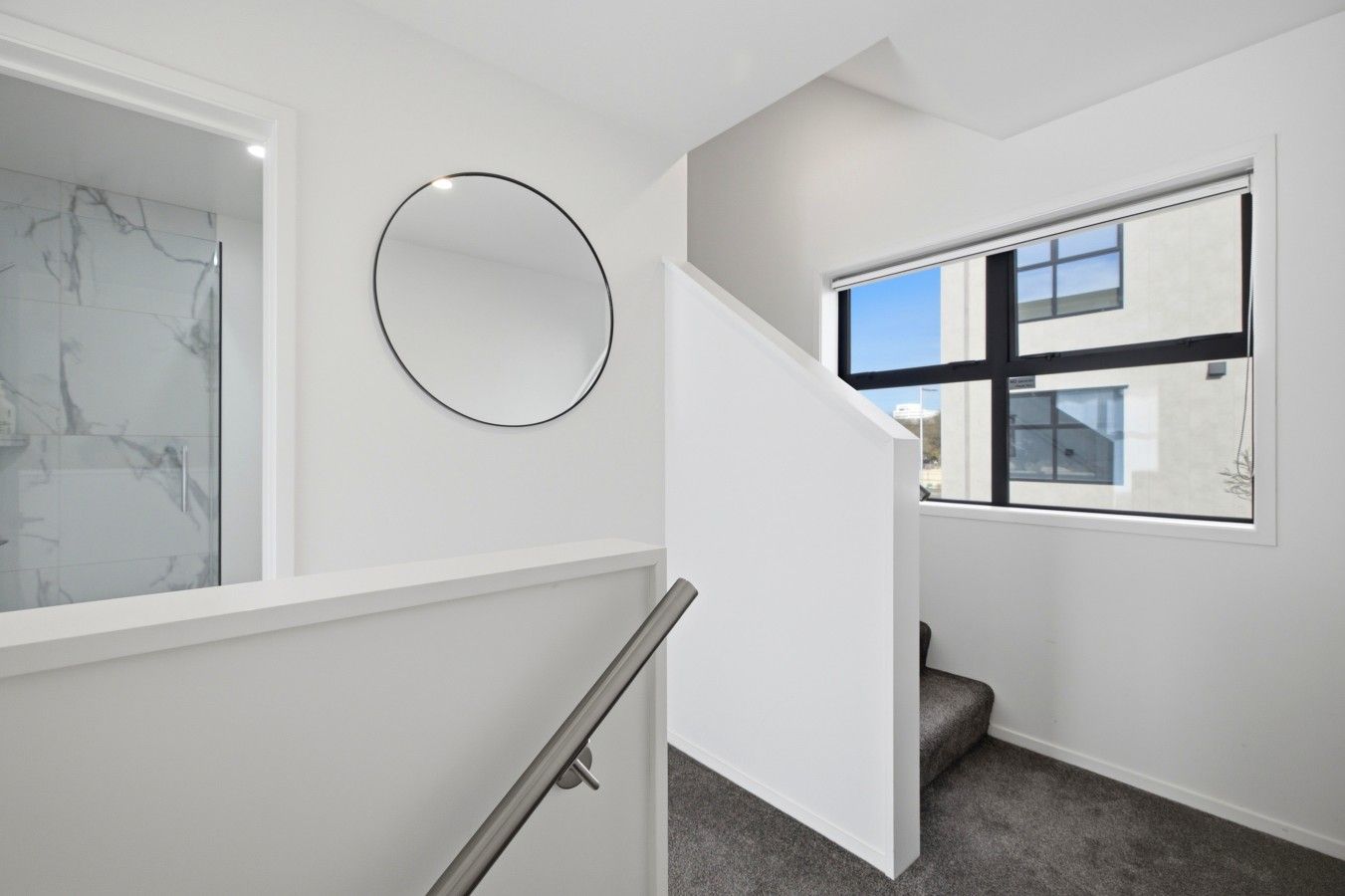 A modern interior with a marble wall, a circular mirror, and a staircase with a glass railing.