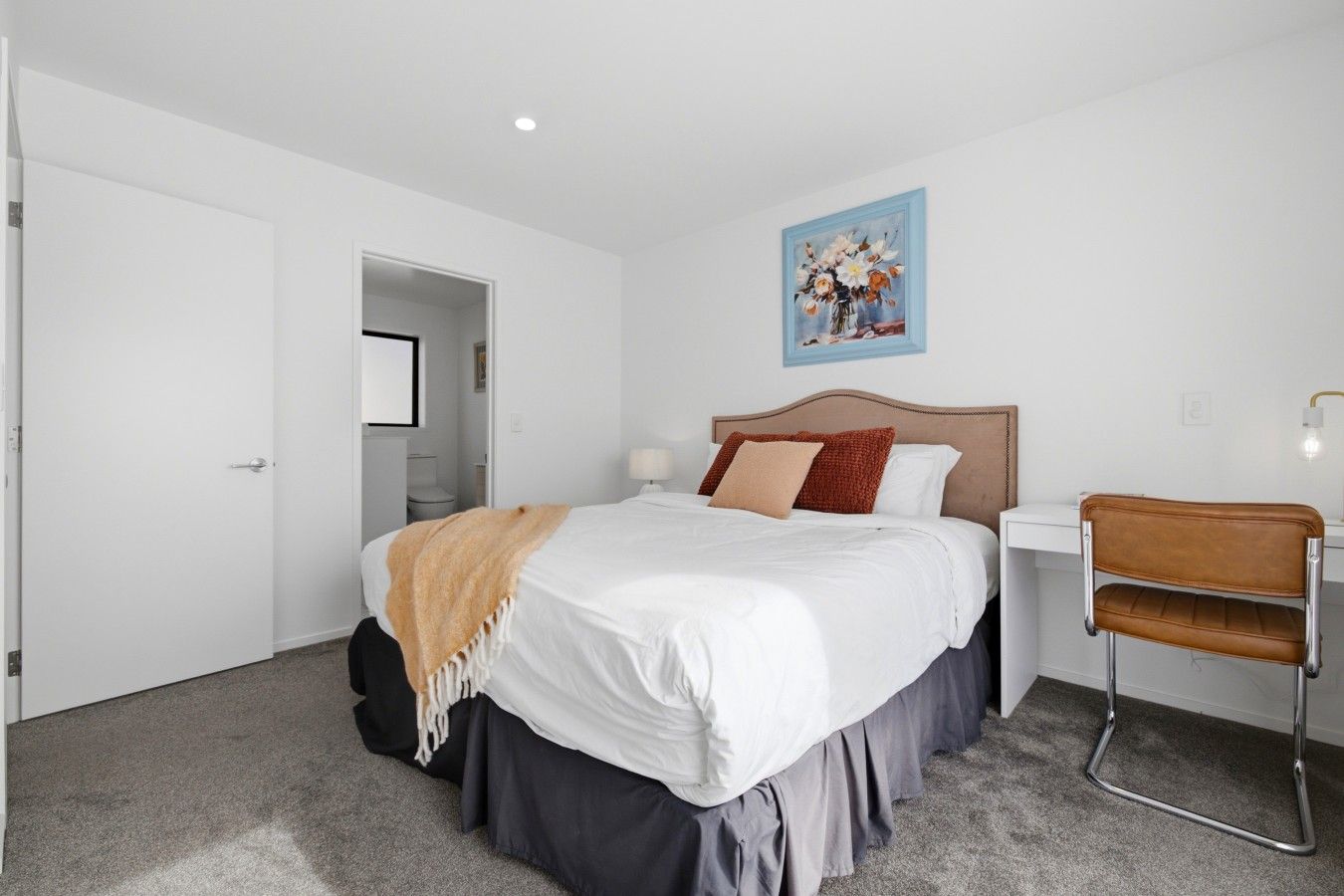 A bedroom with a bed, a chair, a painting, and a door.