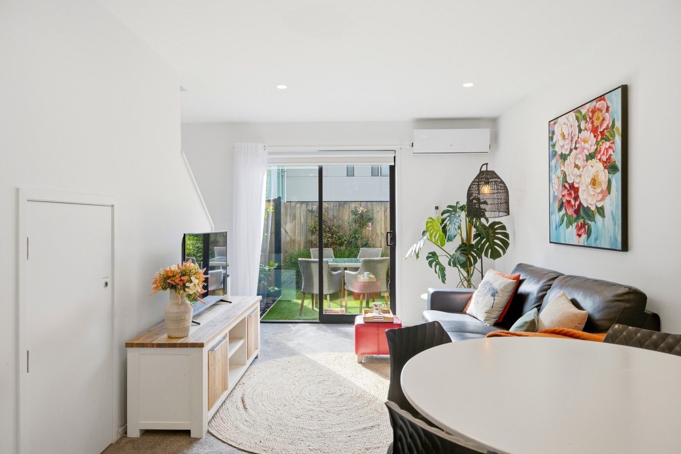 Un salon moderne avec un canapé, une table à manger et un téléviseur. Une porte-fenêtre coulissante donne accès à un jardin.