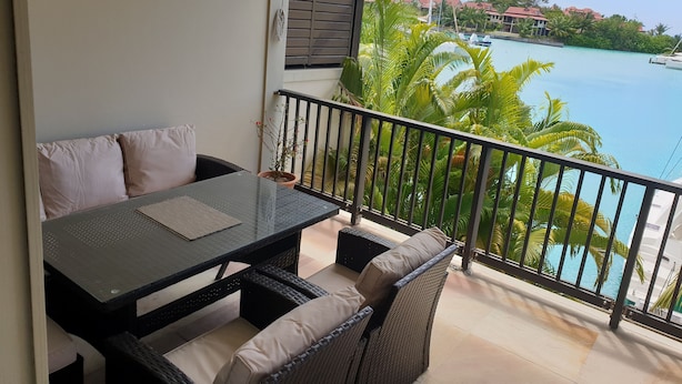Un balcón con mesa y sillas, con vistas a una piscina y paisaje tropical.