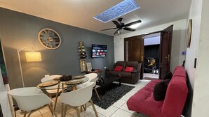 Ein kompakter Wohnraum mit Essbereich, einem roten Sofa, Deckenventilator und einem an der Wand befestigten Fernseher.