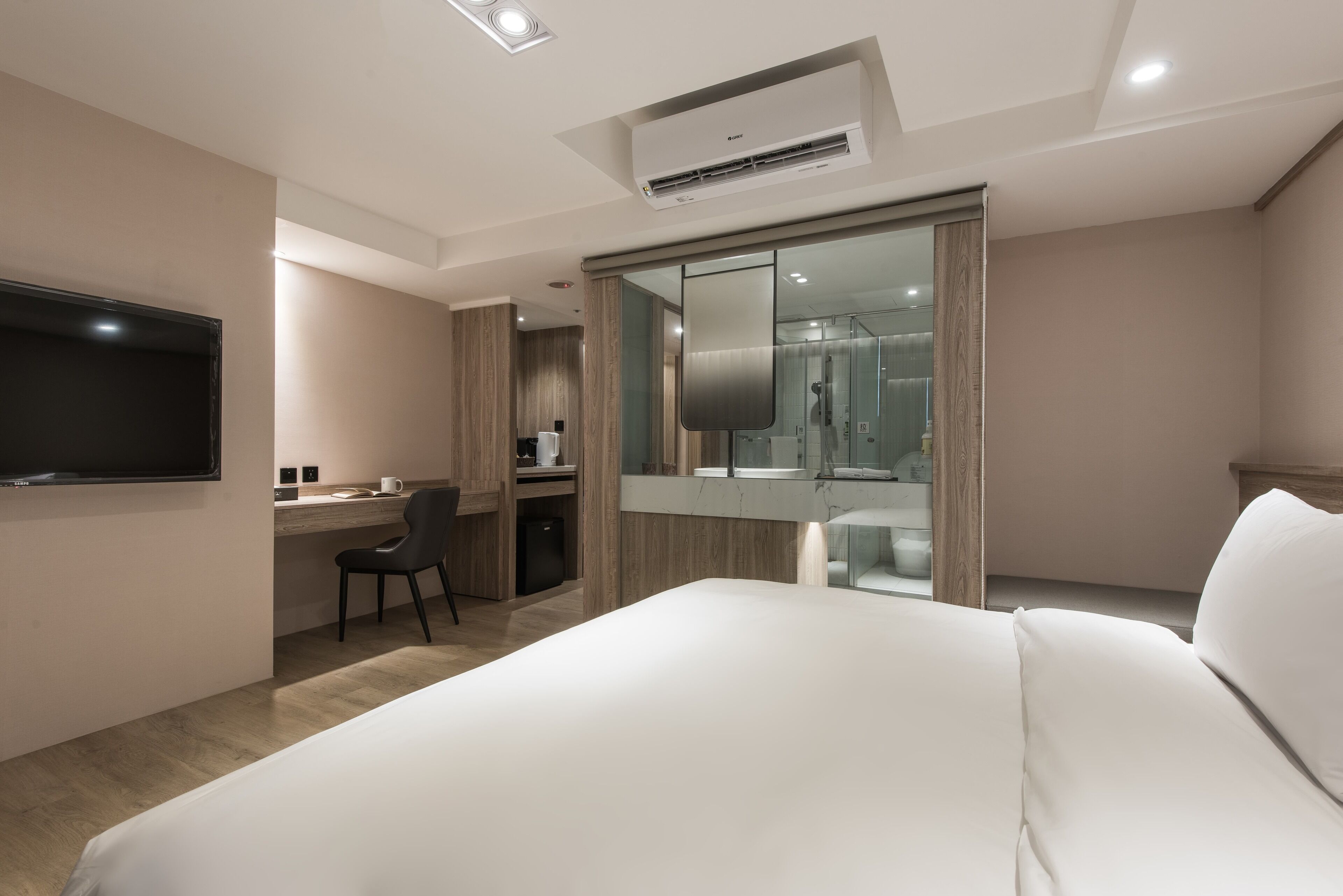 A modern hotel room with a large bed, a desk with a chair, a flat-screen TV, a shower area, and a large mirror.