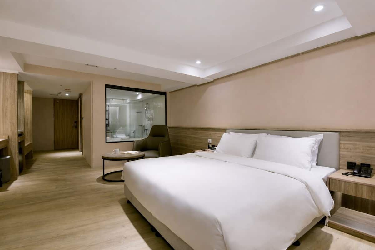 Ein Hotelzimmer mit einem großen Bett, einer Sitzecke mit einem Sessel, einem kleinen Tisch und einem Spiegel.