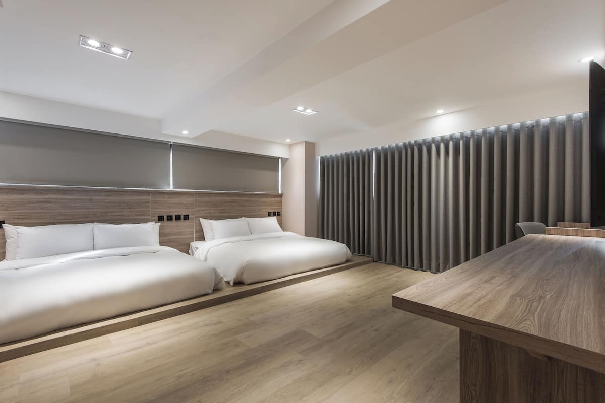 Ein modernes Hotelzimmer mit zwei Betten, einem Holzkopfende, einem großen Fenster mit Vorhängen und einem Holzesstisch.