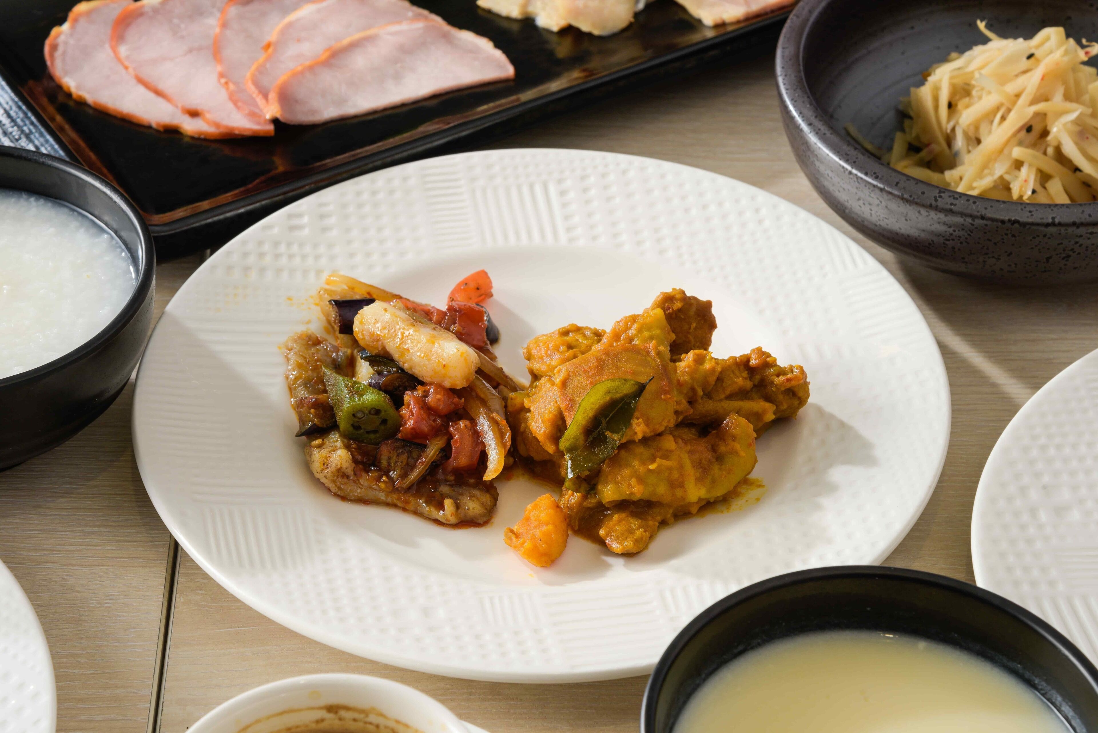 A dining table with various dishes including sliced ham, a plate with mixed vegetables, and bowls of soup.