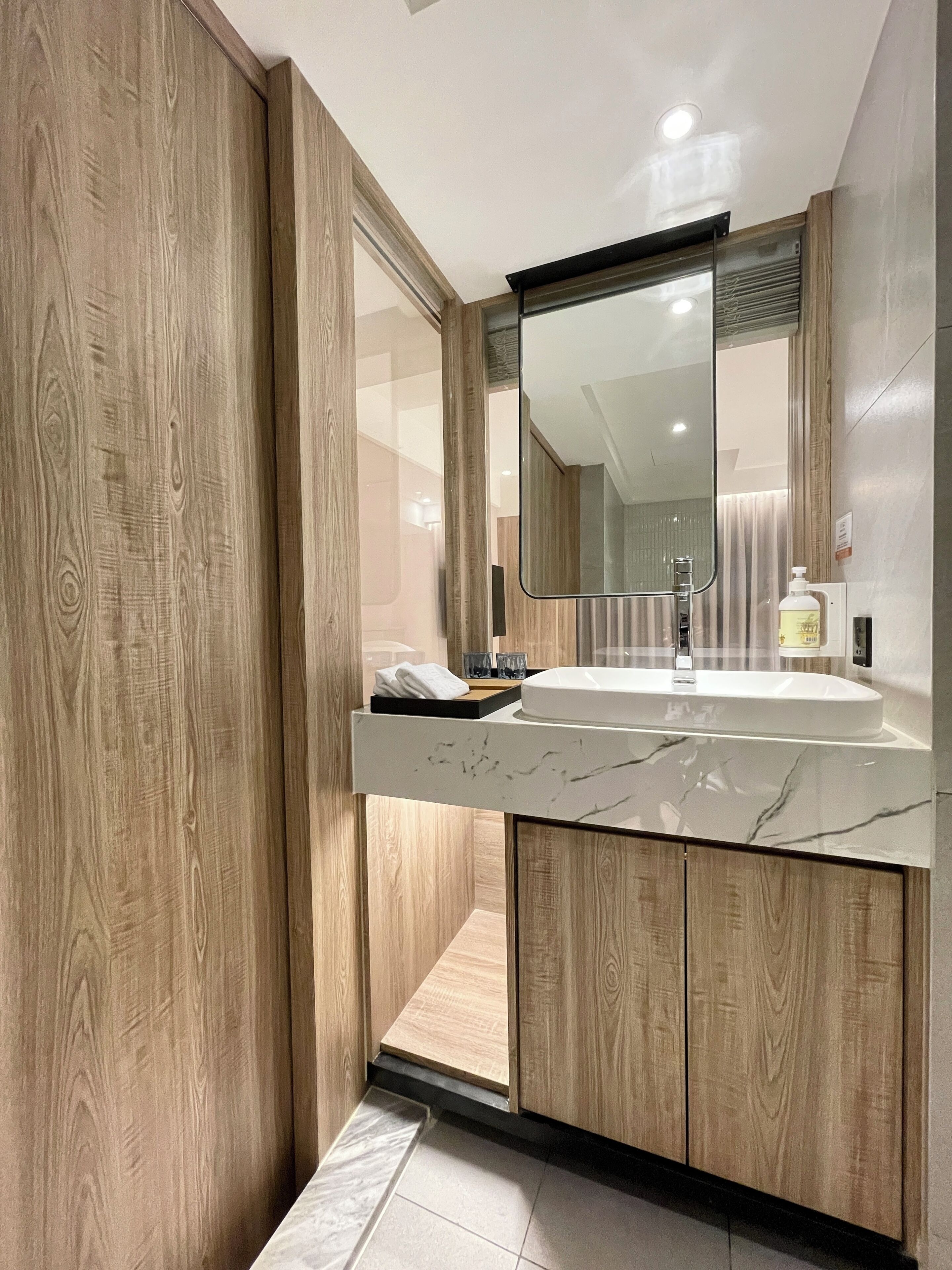 A modern bathroom with a wooden vanity, a marble sink, and a large mirror.