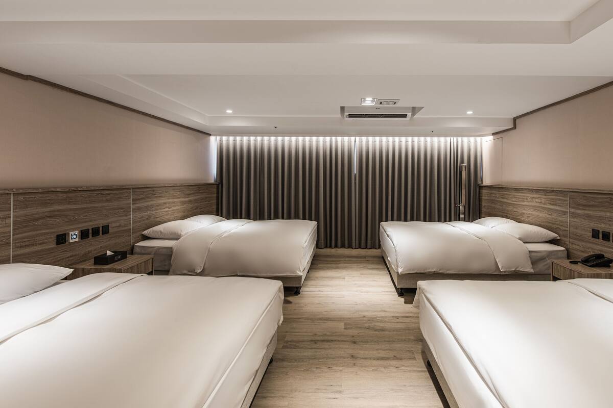 Ein Hotelzimmer mit zwei Betten, einem hölzernen Kopfteil, einem Nachttisch mit Telefon und einem Vorhang mit vertikalem Streifenmuster.