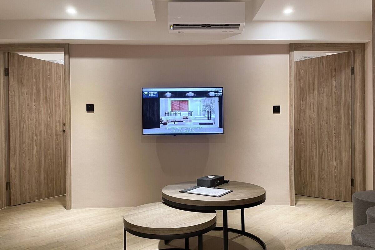 Ein modernes Hotelzimmer mit einem wandmontierten Flachbildfernseher, einem kleinen runden Tisch mit einem Stuhl und Holztüren.
