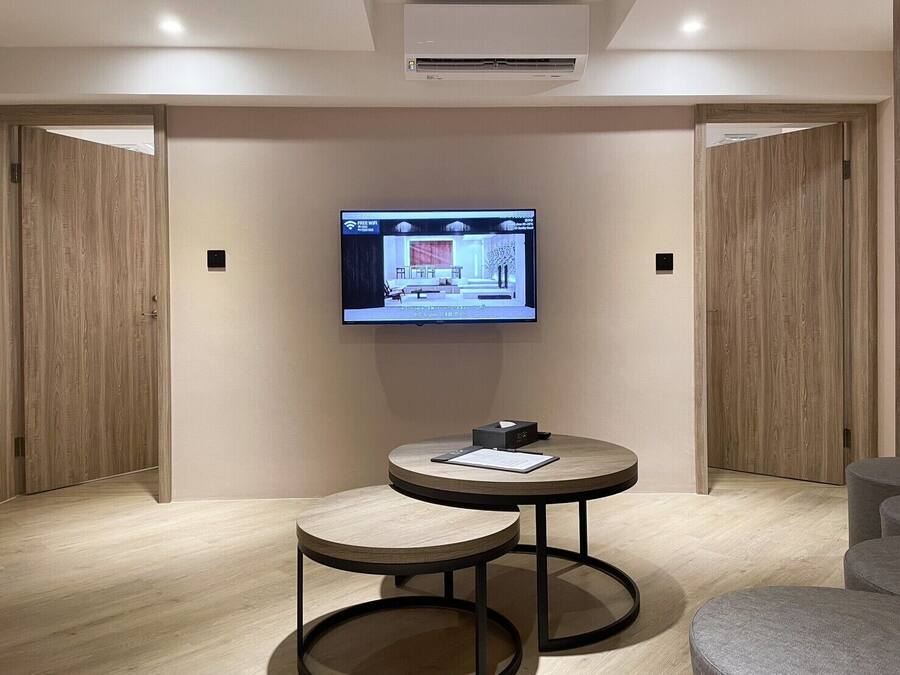 A modern hotel room with a flat-screen TV mounted on the wall, a small round table with a chair, and wooden doors.