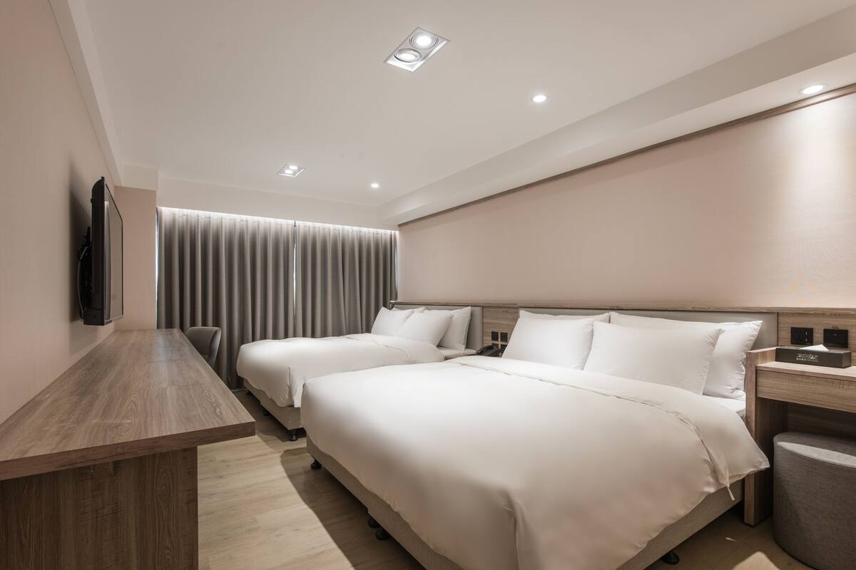 Ein Hotelzimmer mit zwei Betten, einem Schreibtisch, einem Fernseher und einem modernen Deckenstil.