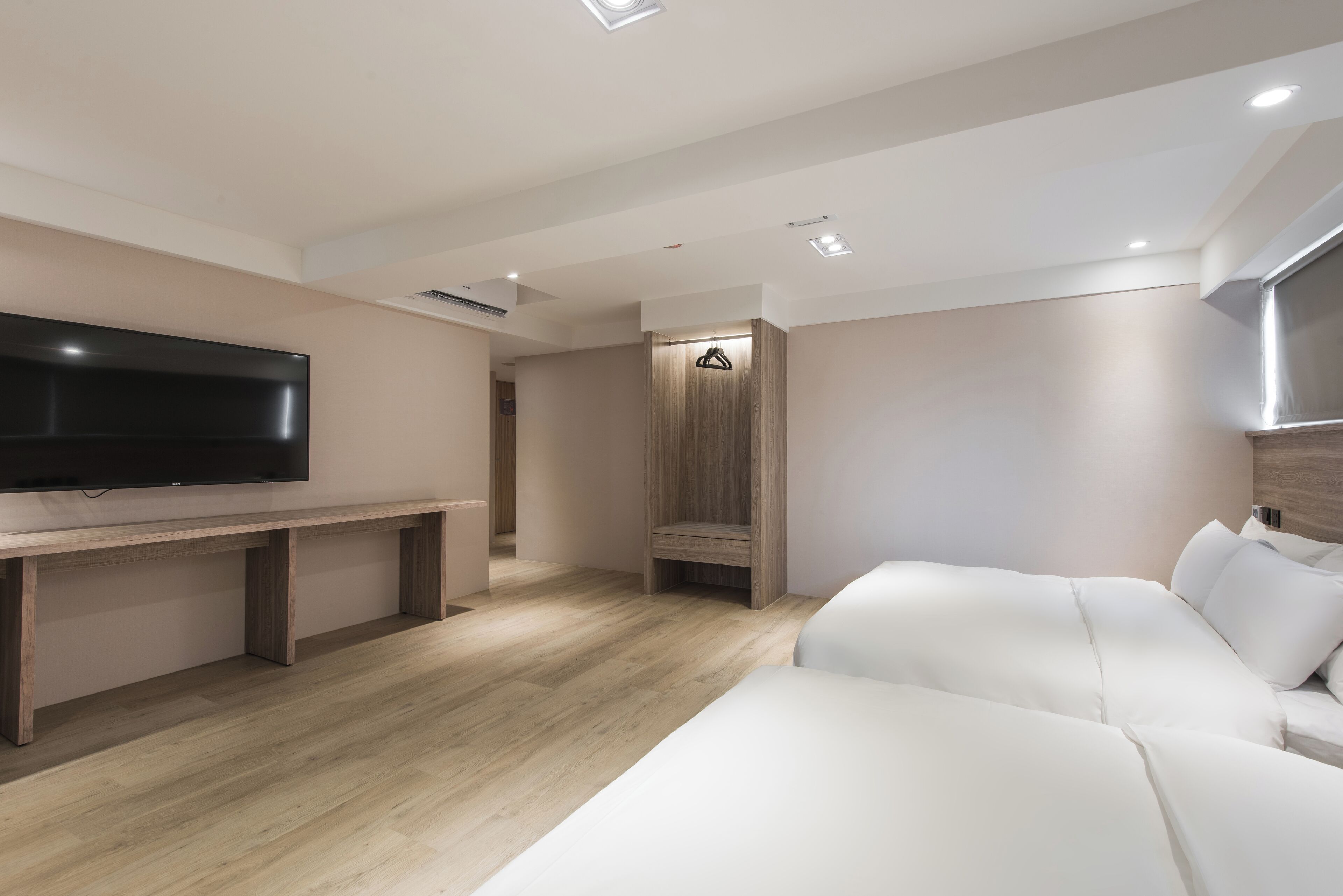 Et moderne hotelværelse med et stort fladskærms-tv, en træbænk, en hvid sofa og et walk-in closet.