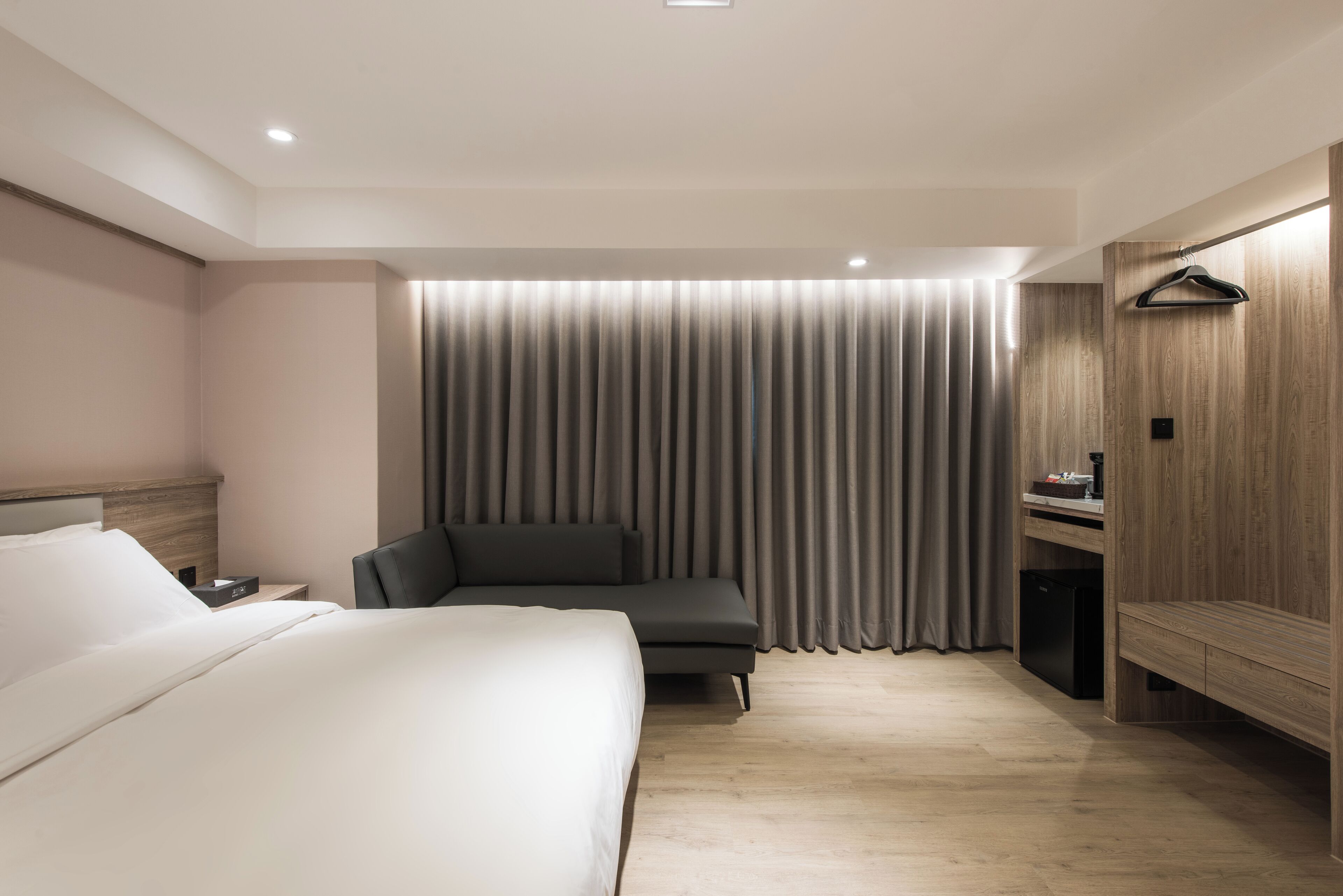 A modern hotel room with a large bed, a desk with a chair, and a wardrobe.
