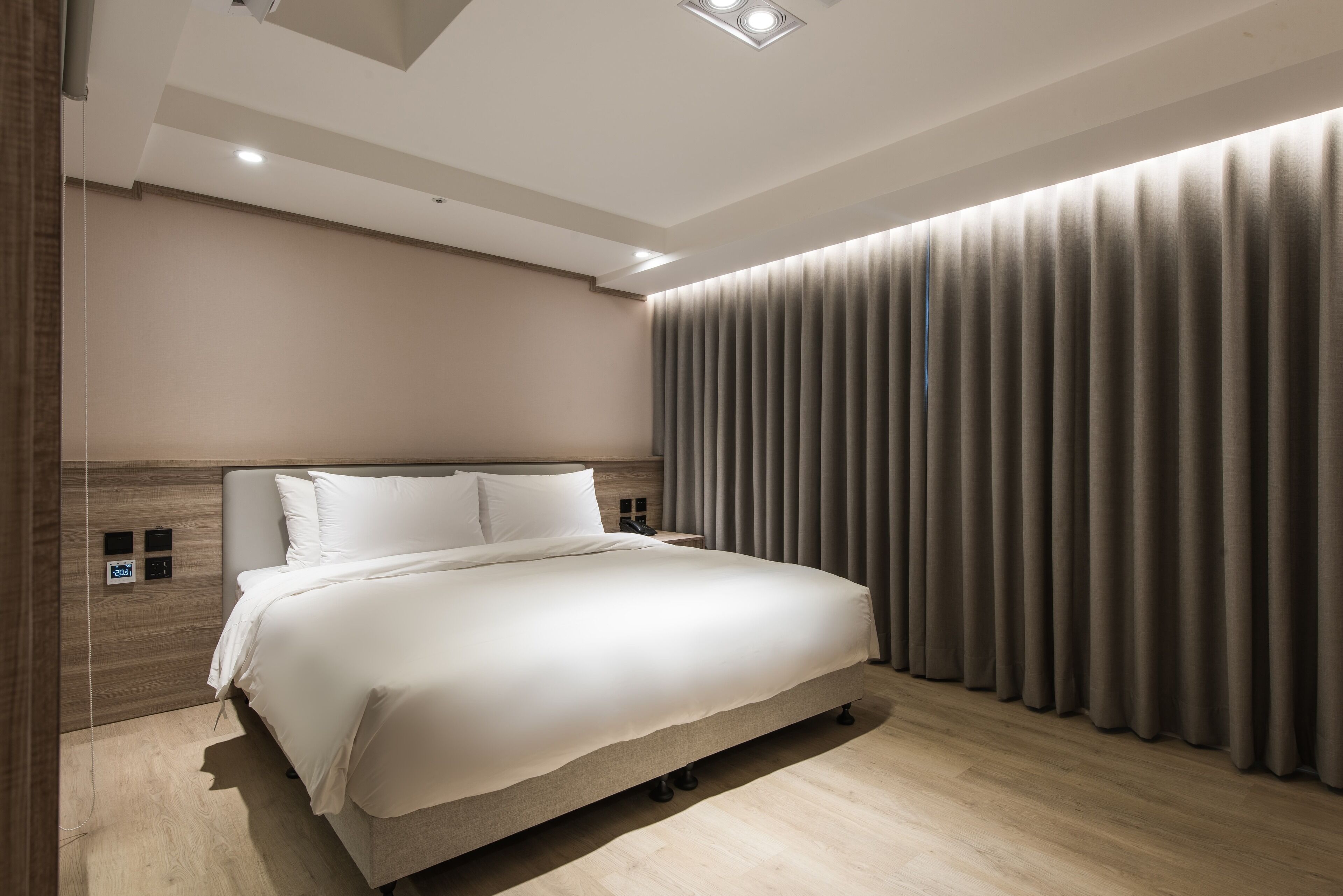 A modern bedroom with a large bed, a wooden headboard, a bedside table, and a curtain-covered window.