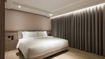 A modern bedroom with a large bed, a wooden headboard, a bedside table, and a curtain-covered window.