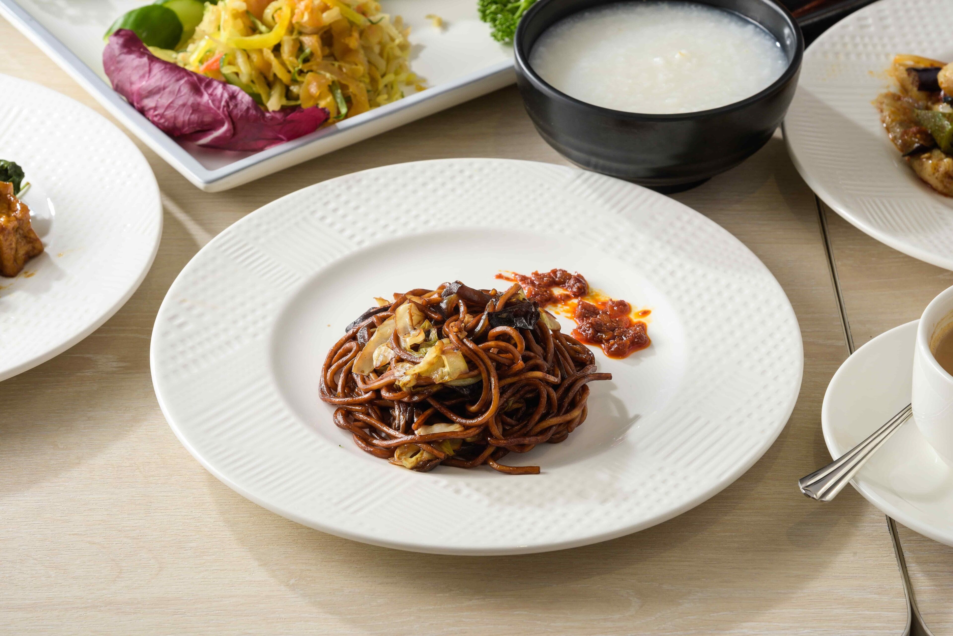 Un tavolo da pranzo con diversi piatti, tra cui noodles, verdure e una ciotola di zuppa.