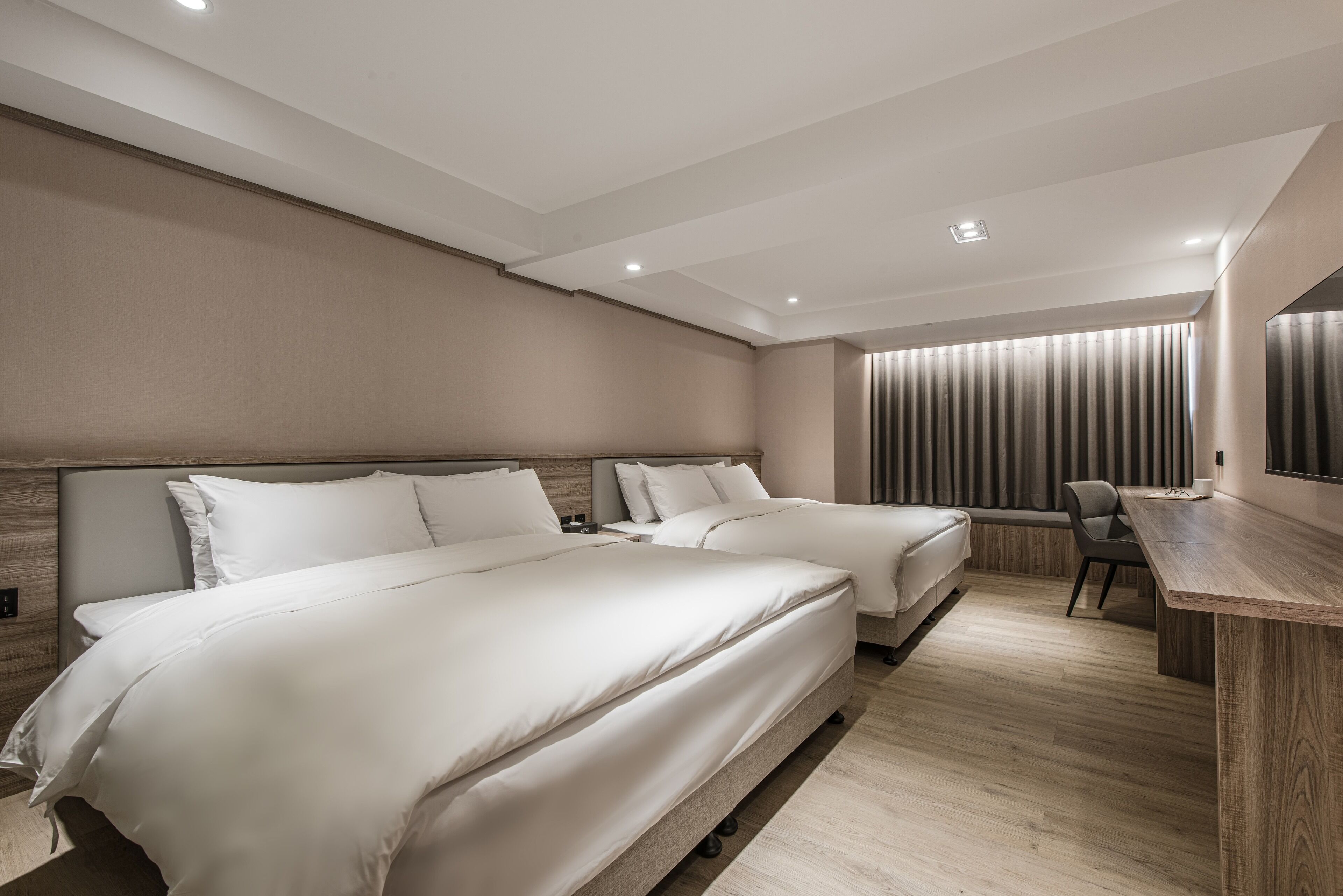 Ein modernes Hotelzimmer mit zwei Betten, einem Schreibtisch und einem Sessel.