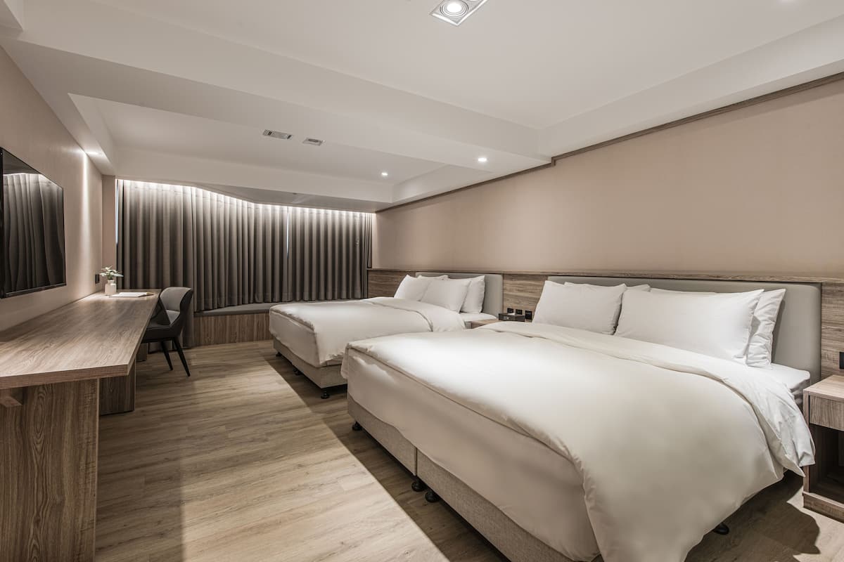 Ein modernes Hotelzimmer mit zwei Betten, einem Schreibtisch und einem großen Fenster mit Vorhängen.