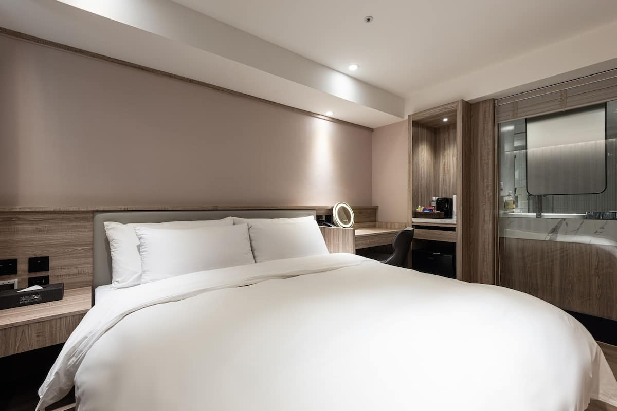 Ein modernes Hotelzimmer mit einem großen Bett, einem Schreibtisch mit Computer, einem Spiegel und einem Badezimmer mit Badewanne.
