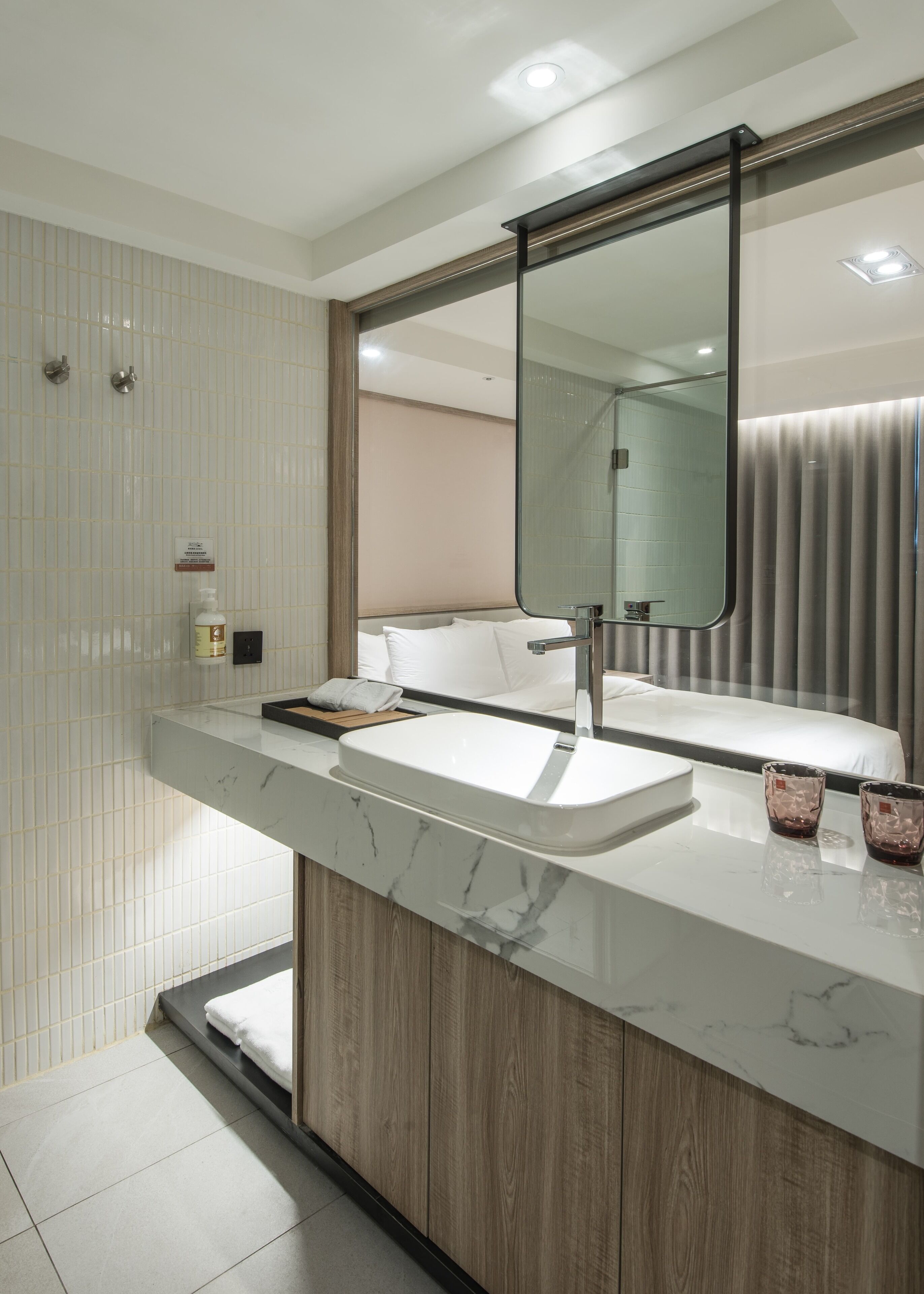 A modern bathroom with a large mirror, a white sink, and a wooden vanity.