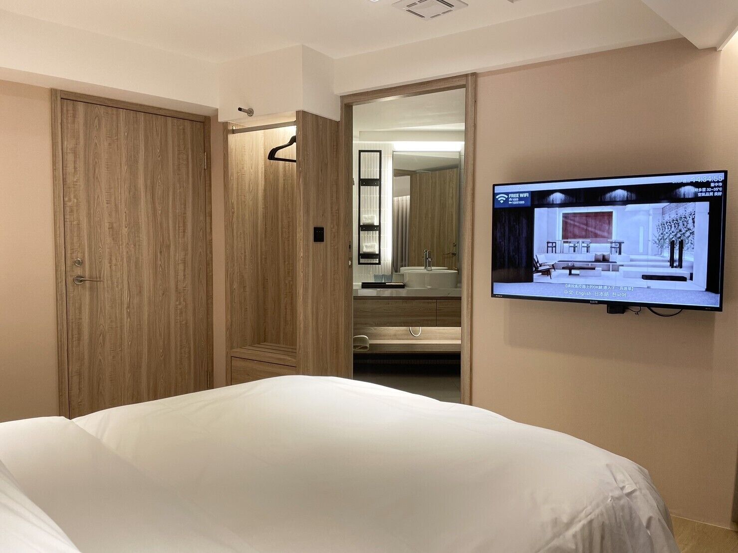 Una habitació d'hotel amb un llit, una televisió penjada a la paret i un armari de fusta.