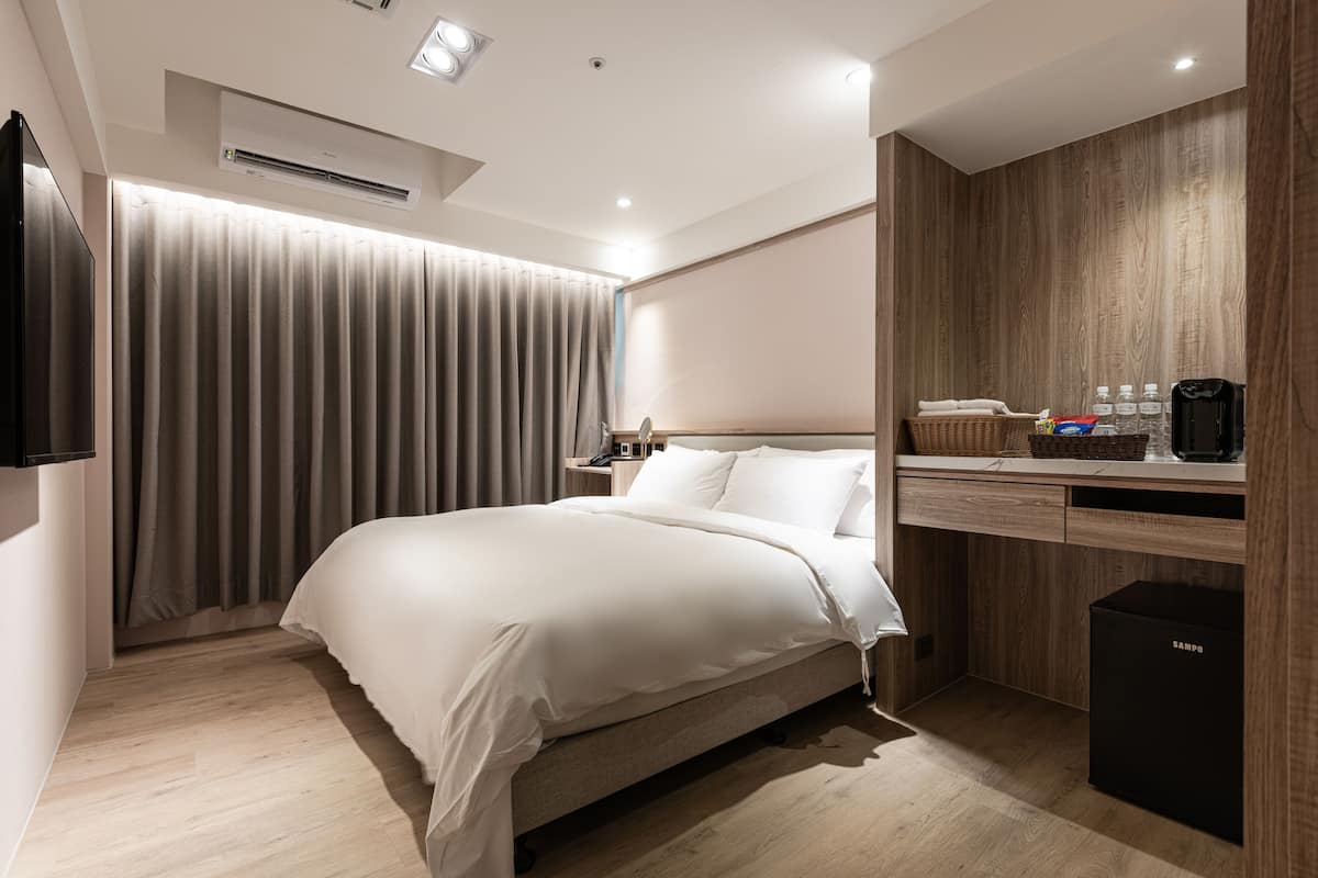 Ein modernes Hotelzimmer mit einem großen Bett, einem Holztisch, einem Flachbildfernseher und einer Minibar.