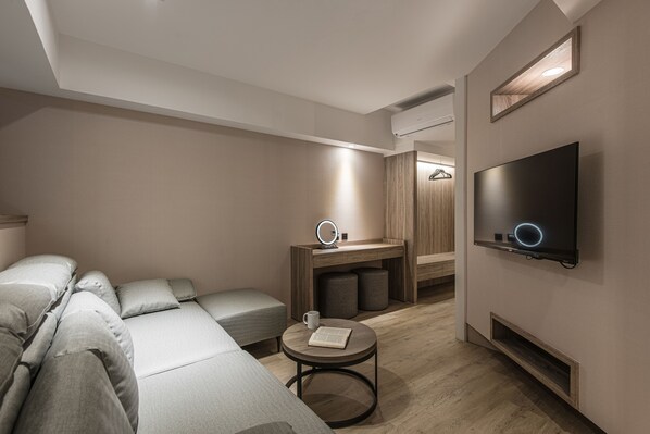 A modern hotel room with a sofa, a small round table, a TV, and a vanity with a mirror. - Spring's Rhapsody Hotel (Taichung)
