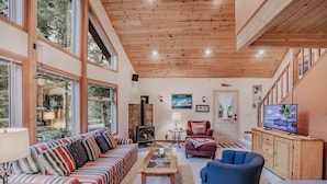A cozy living room with a wooden ceiling, large windows, a fireplace, and a television. - 75sl - 2-bdrm - Loft - Sleeps 6 - Wifi - Pets Ok (Deming)