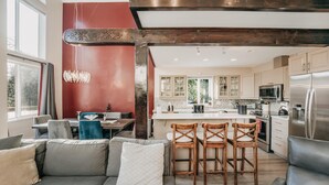 A modern kitchen with a central island, wooden chairs, and a dining area with a sofa and table. - 80mbr - Hot Tub - Wifi - BBQ - Wood Stove - Sleeps 7! (Deming)