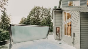 A hot tub with a wooden deck, surrounded by a house with a satellite dish and a window. - 80mbr - Hot Tub - Wifi - BBQ - Wood Stove - Sleeps 7! (Deming)