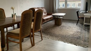 A living room with a brown leather sofa, a wooden dining table with chairs, a small coffee table, and a patterned rug. - Mitten im Herzen von Hannover (Hannover)