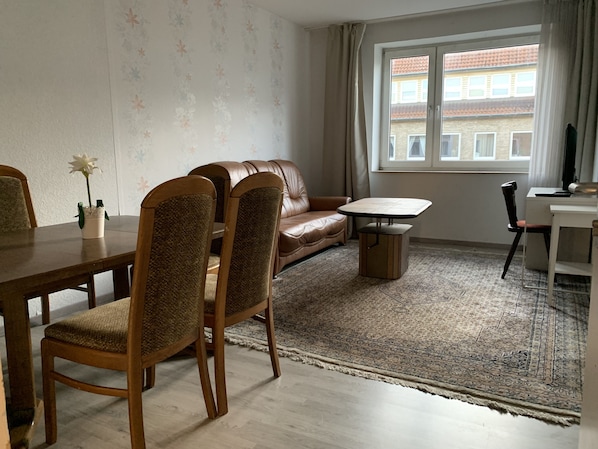 Ein Wohnzimmer mit braunem Ledersofa, einem Holzesstisch mit Stühlen, einem kleinen Couchtisch und einem gemusterten Teppich.