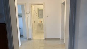 Een schone, goed verlichte hal met een 'WELCOME' mat die naar een badkamer leidt, met een wastafel en spiegel.