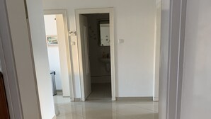 A clean, well-lit hallway with a 'WELCOME' mat at the entrance, leading to a bathroom with a sink and a mirror. - Mitten im Herzen von Hannover (Hannover)