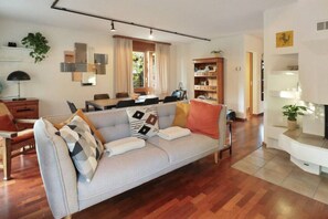 Una sala de estar moderna con un sofá gris, piso de madera y una zona de comedor con una mesa y sillas.