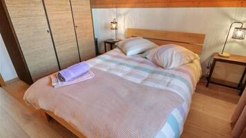 A neatly made bed with a striped blanket, two pillows, and a folded towel on the bed. There are two bedside tables with lamps, a wooden wardrobe, and a wooden headboard.