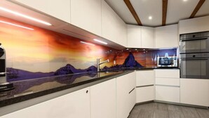 Una cocina moderna con armarios blancos, una encimera de granito y un salpicadero que representa un paisaje de montaña.