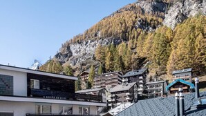 Un complejo turístico de montaña con edificios modernos, incluyendo un hotel con balcones y vistas al bosque y a la montaña circundante.