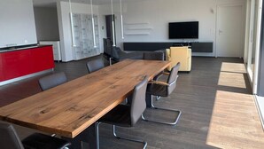 Ein moderner Konferenzraum mit einem Holztisch, grauen Stühlen und einer roten Küchenzeile im Hintergrund.
