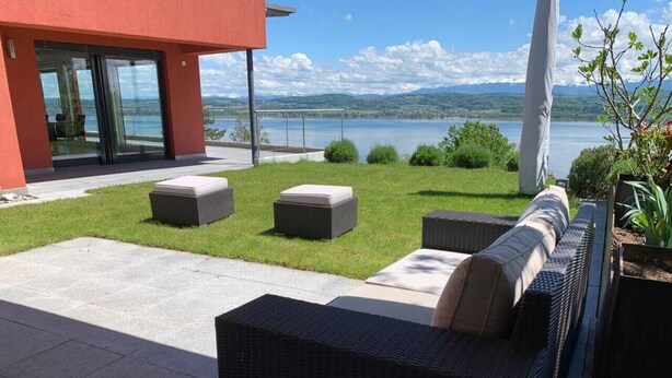 Eine Terrasse mit Korbmöbeln und Blick auf einen See.