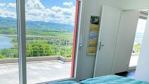 Ein Schlafzimmer mit einem großen Fenster, einem Bett mit grüner Bettwäsche und Blick auf einen See und Berge.