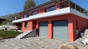 Ein modernes, zweistöckiges Haus mit roter Fassade, einem Balkon und einer Garage mit zwei Toren.