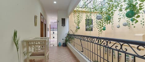 Un pasillo con una silla blanca, plantas en macetas y un balcón con barandilla de metal.