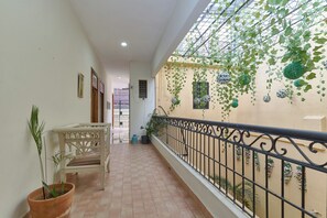 A corridor with a white chair, potted plants, and a balcony with a metal railing. - Hotel Anabella (Santo Domingo)